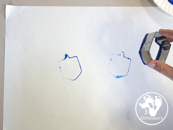 Hanukkah Stamping Painting with Cookie Cutters is a great Hanukkah craft you can do with different ages. And a fun mix of Hanukkah themes you can find in the cookie cutters.