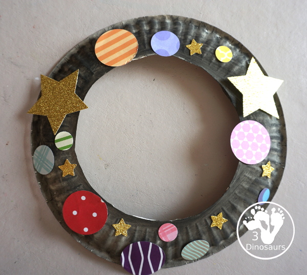 Scrapbook Paper Space Wreath Craft - a fun space craft for kids that is made with a paper plate, craft punches that are circles and stars with glitter paper and scrapbook paper. It makes a fun space craft. - 3Dinosaurs.com